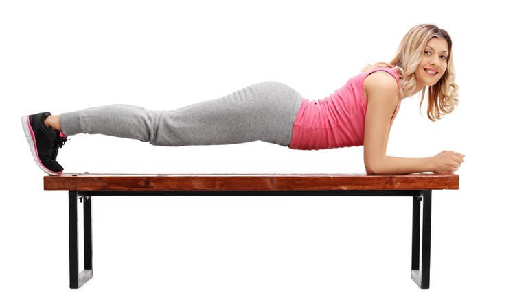 Studio shot of a young woman exercising in plank position on a wooden bench isolated on white background