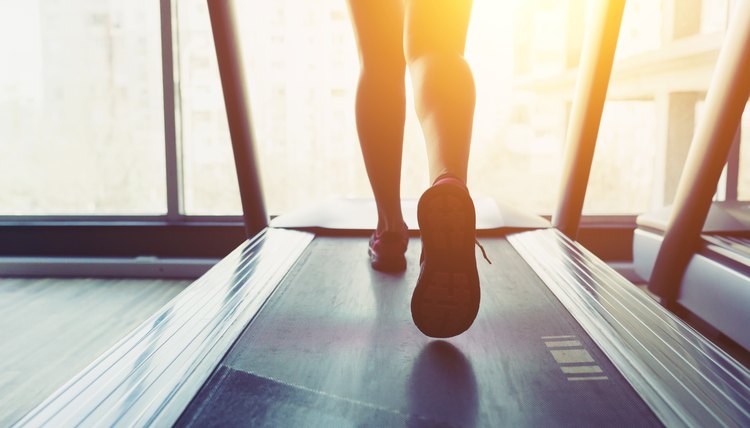 Fitness girl running on treadmill. Woman with muscular legs in gym