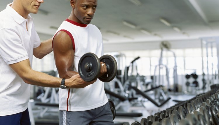 Coach helping a mid adult man exercise with dumbbells