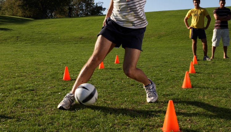 Men practising football, dribbling through cones in field