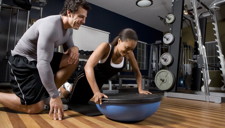 Trainer instructing a young woman on a fitness ball in the gym