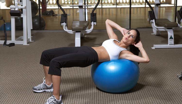 Woman doing exercise on fitness ball in gym, side view