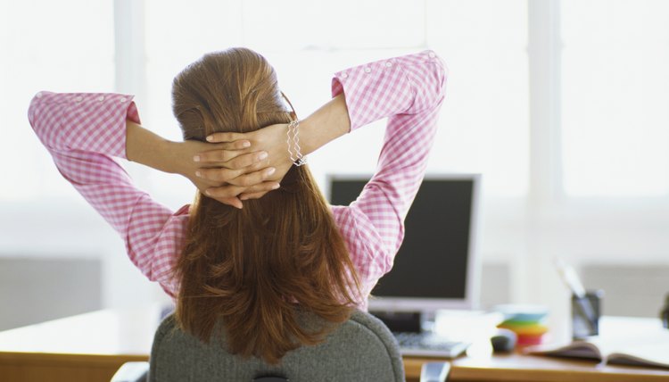 rear view of a businesswoman sitting in front of a computer with her hands behind her head