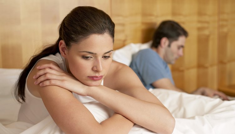 Bored woman sitting in bed with man using laptop by her