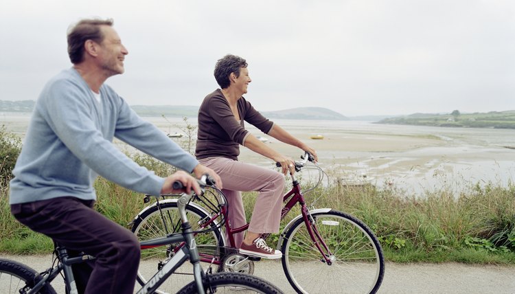 Senior couple riding bicycles by sea, smiling, side view (focus on woman)