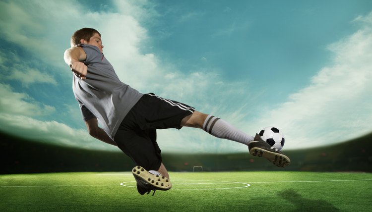 Soccer player kicking the soccer ball in mid air, in the stadium with the sky