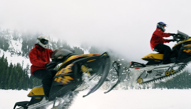 Two people riding snowmobiles, leaping across snow