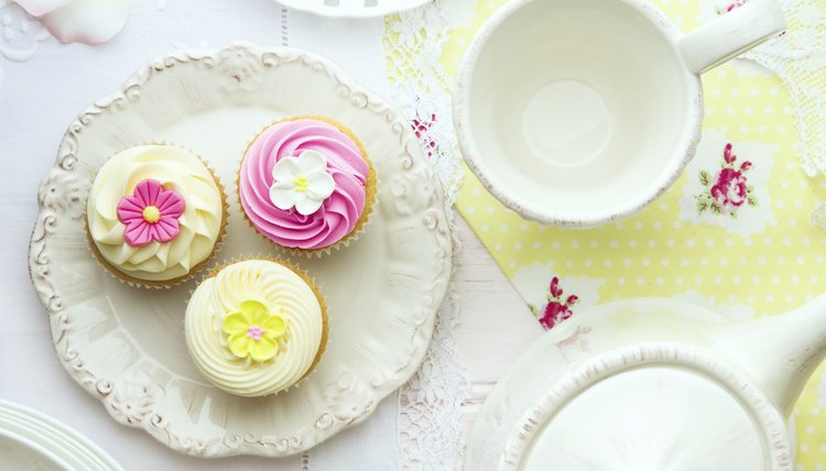 An overhead view of a pretty cupcakes on a plate next to a tea pot and cup.