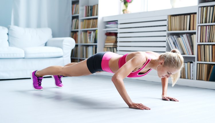 A fit woman exercises at home with push-ups.