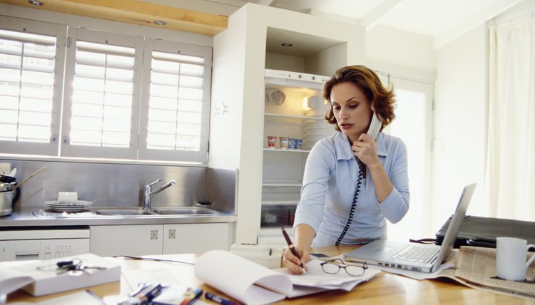 Busy woman in kitchen on telephone and writing notes