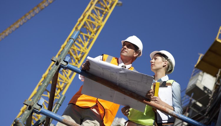 Male and Female Construction Workers Stand on a Platform in a Building Site Discussing a Blueprint