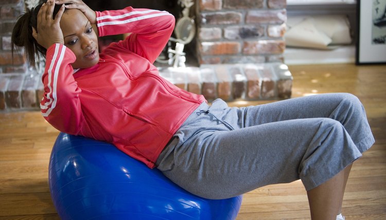 Young woman in sports clothing exercising on fitness ball by fire place