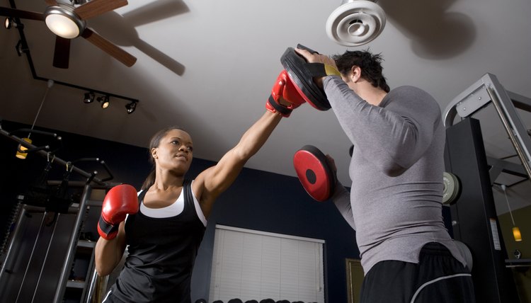 Trainer instructing a young woman with boxing equipment in the gym