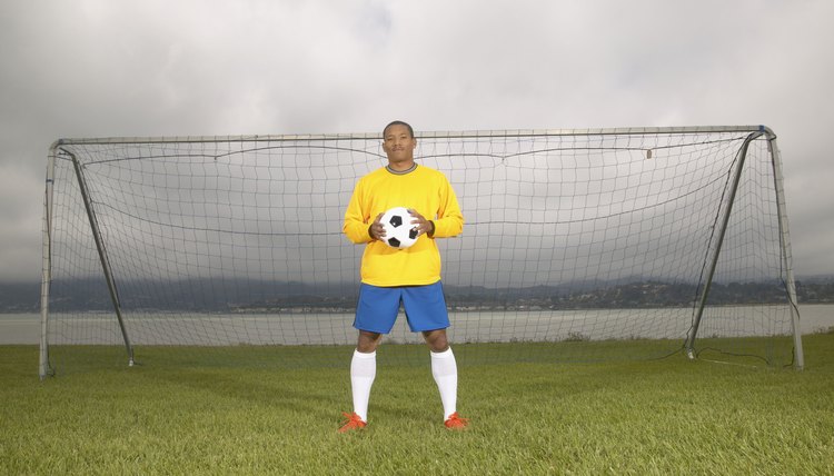 Young male football player standing at a goal post holding a soccer ball