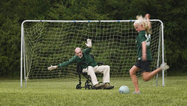 Girl (10-11) playing soccer with grandfather in wheelchair as goal keeper