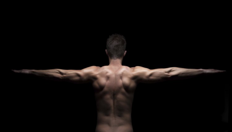 Rear view of a muscular man with arms streched out on black background