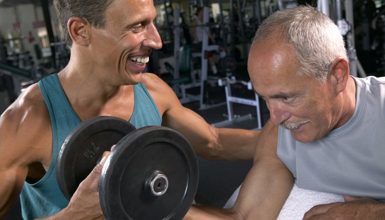 Two mature men in gym, one lifting weights