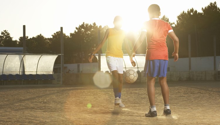 Two boys (11-13) playing football, lens flare