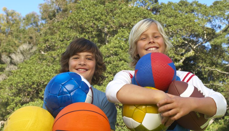Two boys (11-13) holding sport balls outdoors, smiling, portrait, low angle view
