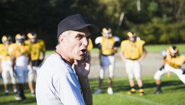 Close-up of a coach on a football field with players playing in the background