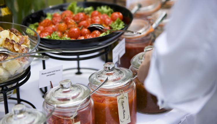 Caterer preparing a salad with dressing on a buffet table.