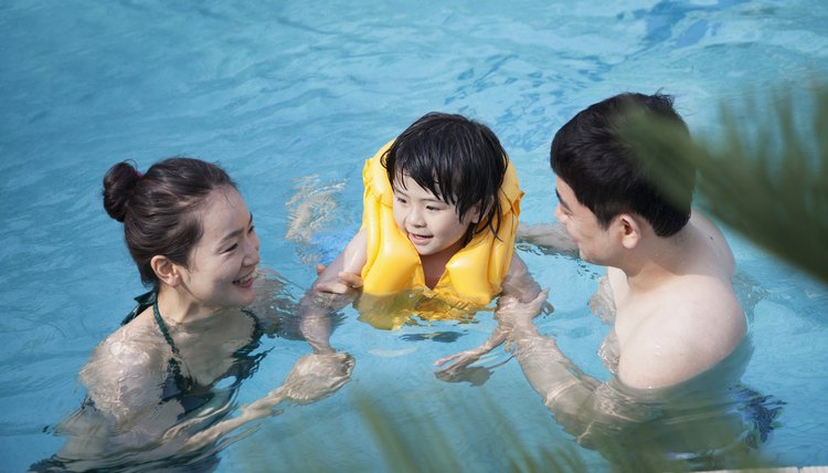 Happy smiling family teaching son how to swim in the pool