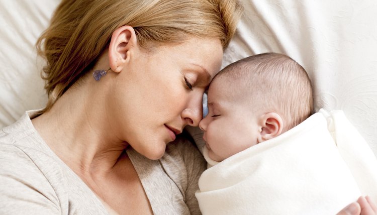 A mother holds her infant while lying in bed.