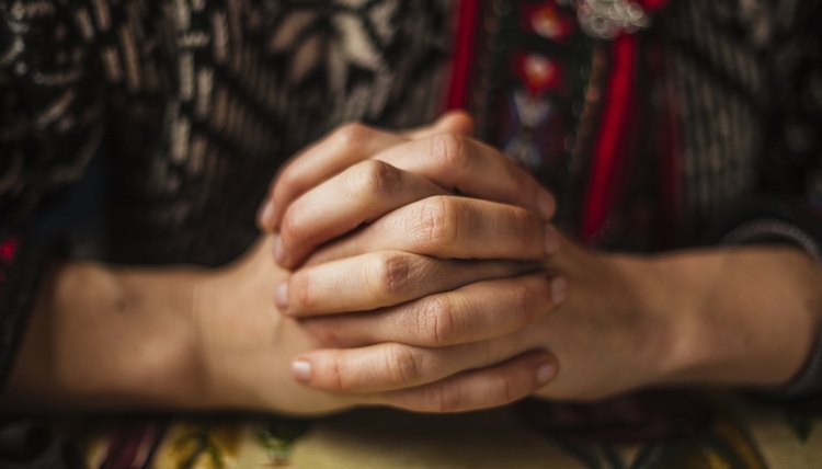 A close-up of a woman clasping her hands in prayer.