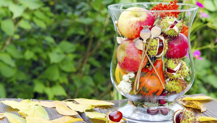 A glass vase filled with seasonal fruit and flowers.