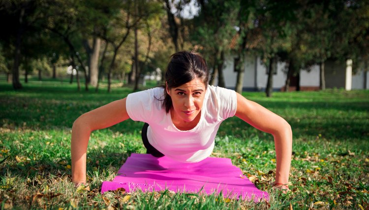 Woman doing push-ups in park on green grass.