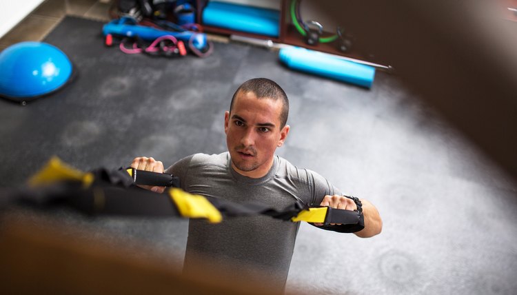 Young man at the gym working on her back on trx