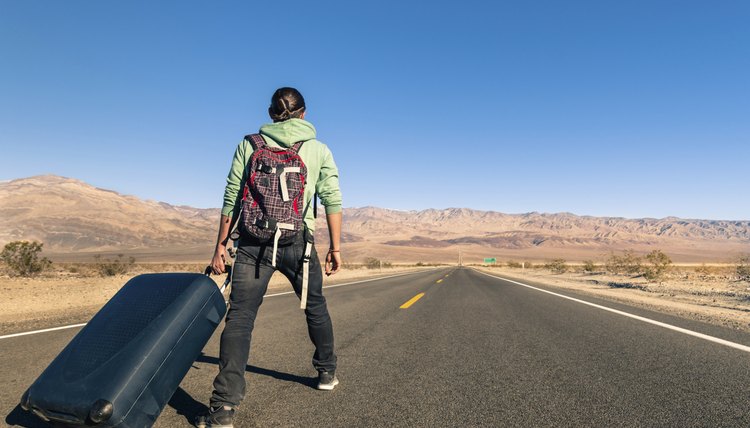 A hobo traveller is walking on an empty road.