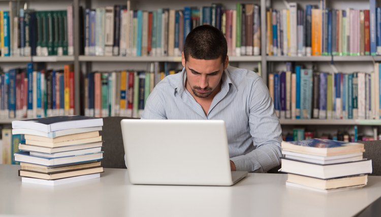 A university student typing on his laptop in a library.
