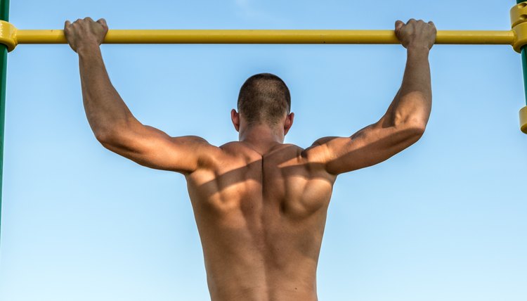 Muscular back of athlete doing pull-up on bars