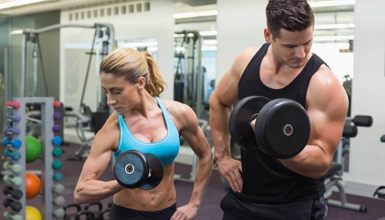 Muscular man and woman lifting dumbbells together