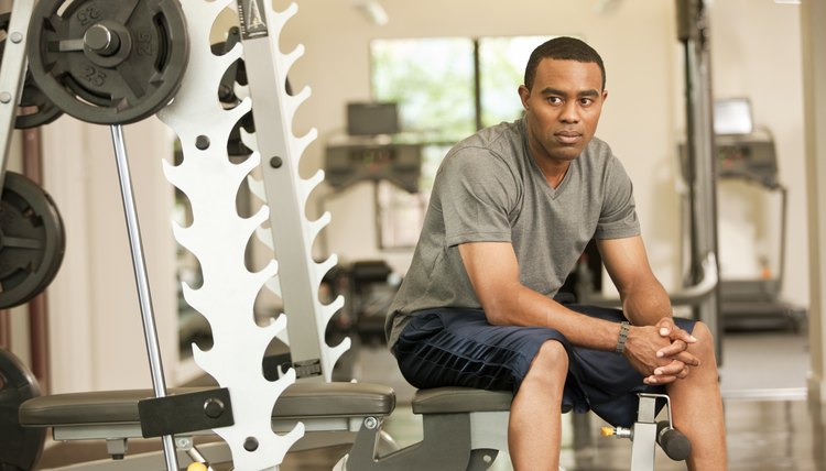 African American man resting in health club on weight-lifting bench