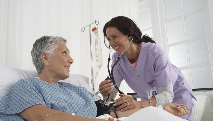 Nurse taking patients blood pressure in hospital bed, smiling