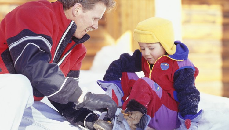 Man helping son (4-5) with snowboard