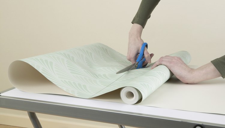 Person cutting through roll of wallpaper