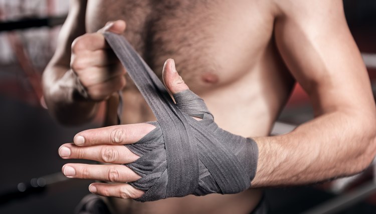 Getting ready. Close up of strong muscular man carefully wrapping his hand with boxing bandage while preparing for training.