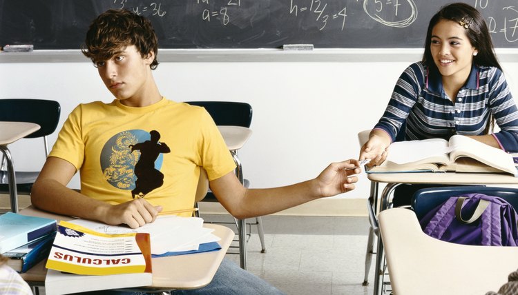 A boy and girl are passing a note back and forth to one another.