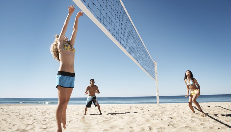 Teenage boy and girls (16-18) playing volley ball on beach