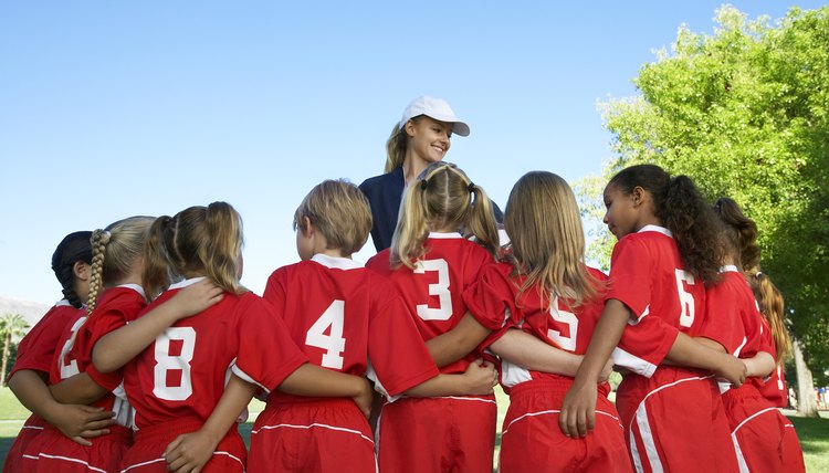 Group of children soccer players embracing standing in front of coach, back view
