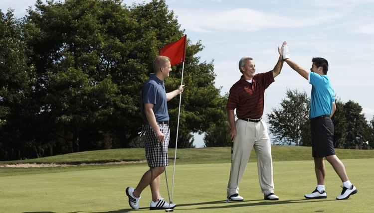 Golfers high fiving on putting green standing next to golfer holding flag