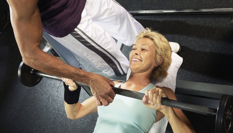 Mature woman lifting weight guided by male instructor, smiling