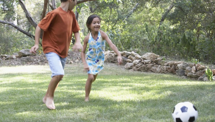 Front profile of a boy and a girl playing football in a garden