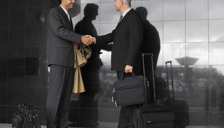Two businessmen shaking hands by luggage, smiling, side view