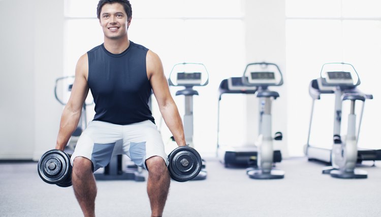 Smiling man doing squats with dumbbells in gymnasium