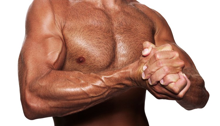 Close-up of a man's chest and arms as he clasps his hands to flex his muscles.