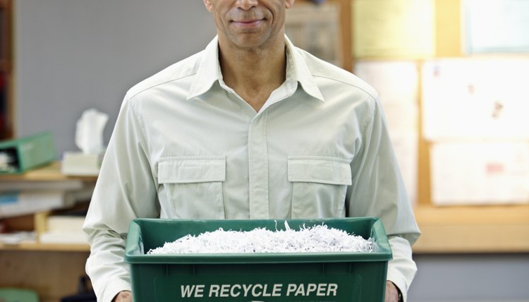 An employee holds a recycling bin for paper in an office.